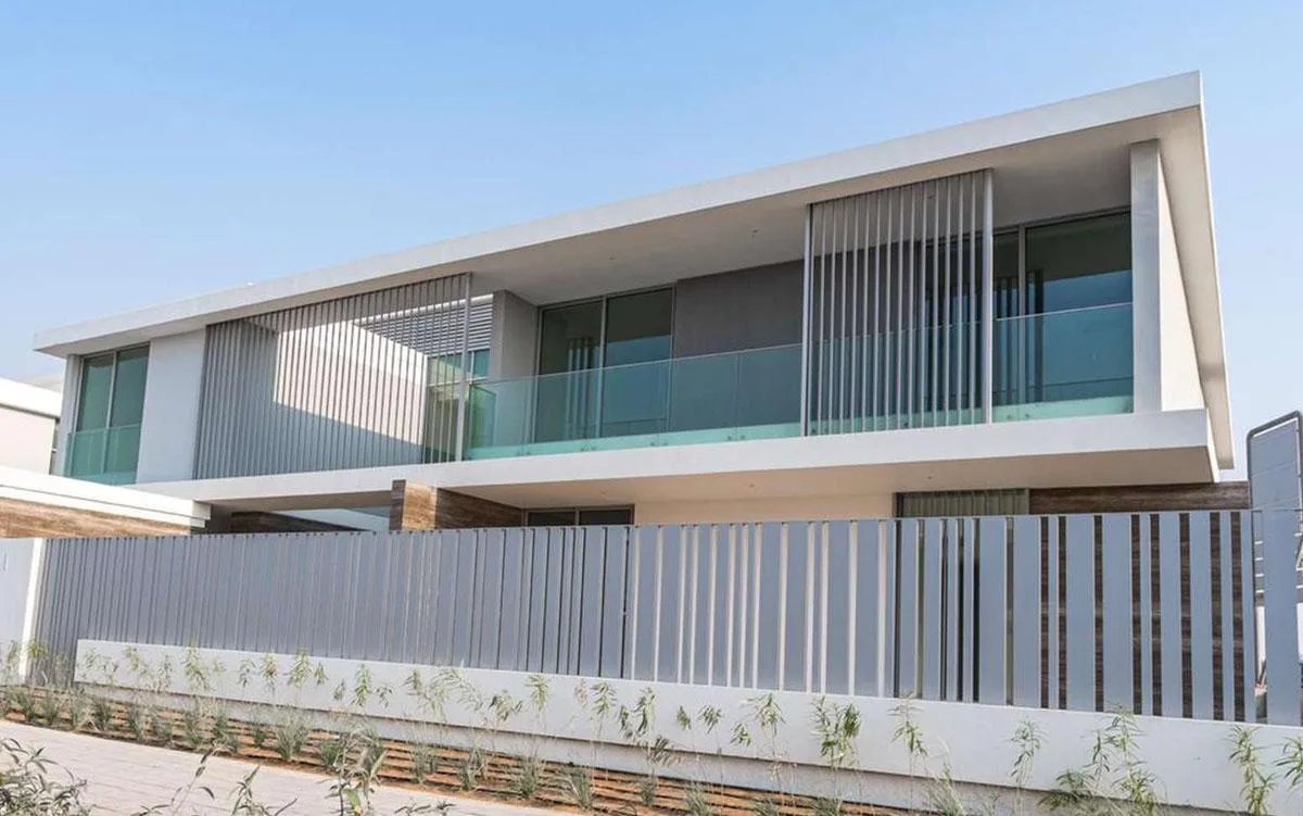 Contemporary villa in Dubai Hills Estate with a cantilevered upper floor, vertical aluminium fins, glass balustrades and a slatted boundary screen.