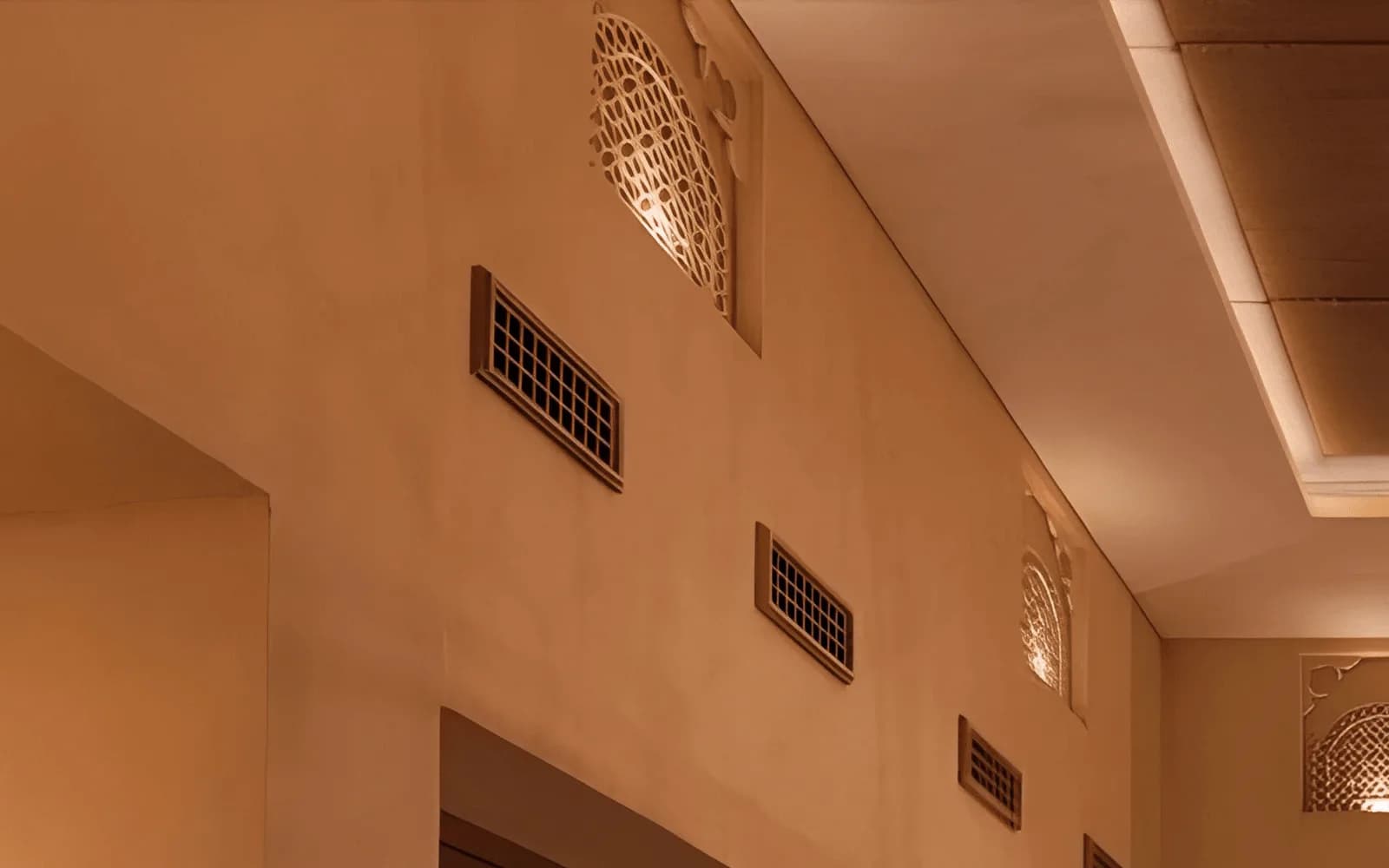 Hand-polished plaster wall with backlit carved gypsum niches, timber grille vents and a cove-lit recessed ceiling raft.