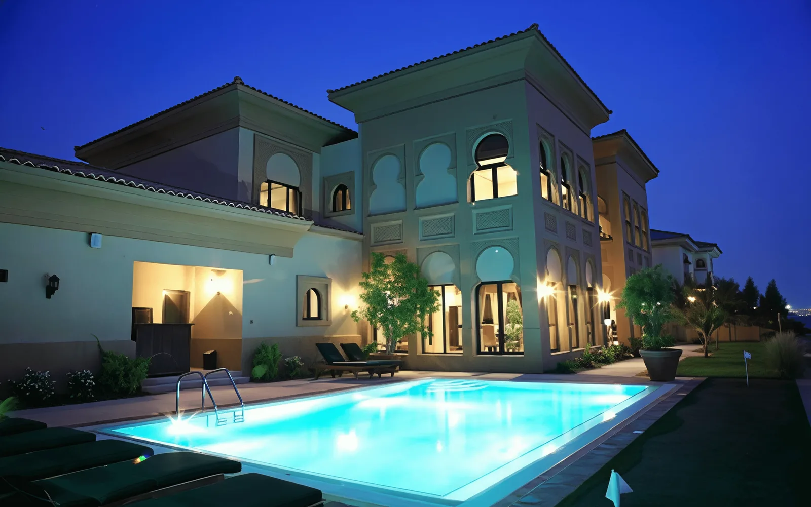 Two-storey villa on Palm Jumeirah at dusk, with arched windows, carved plaster detailing and a lit swimming pool in the foreground.
