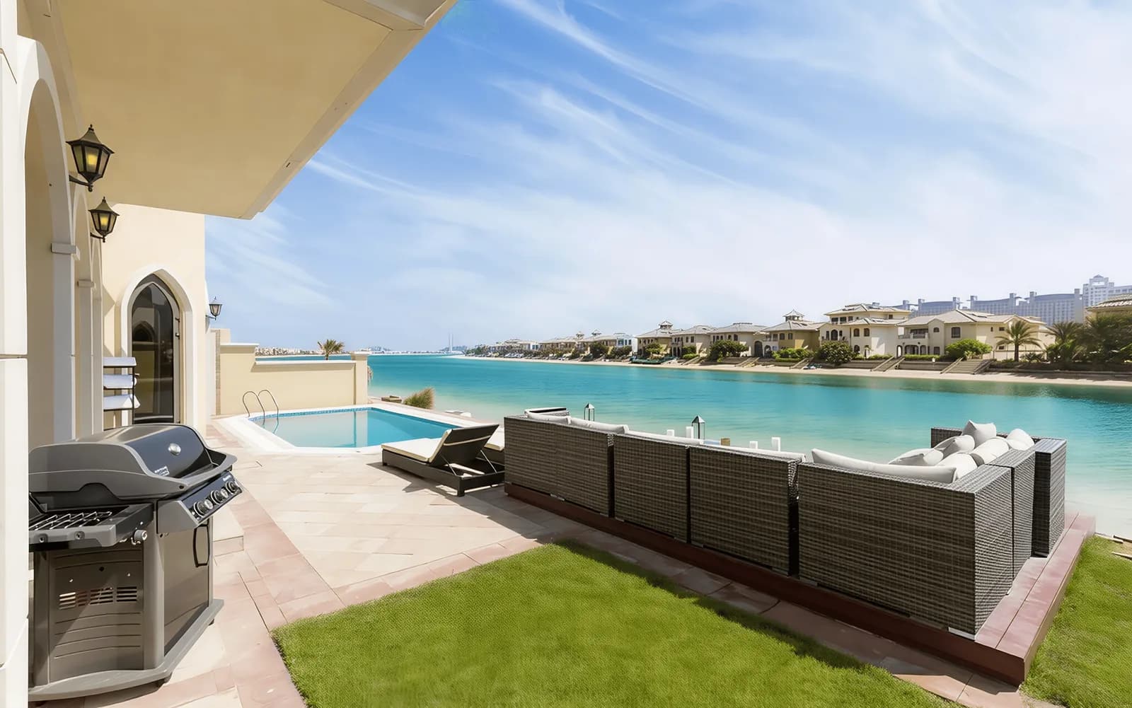 Villa pool terrace with outdoor seating and a sun lounger, looking across a lagoon to a row of waterfront villas.
